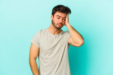 Kafkasyalı genç adam mavi arka planda izole edilmiş bir şekilde bir şeyi unutuyor. Alnına avuç içi ve gözlerini kapayarak vuruyor..