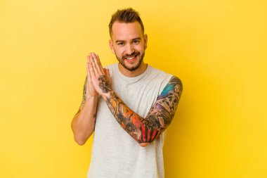 Sarı arka planda izole edilmiş genç dövmeli beyaz adam enerjik ve rahat hissediyor, ellerini ovuşturuyor..