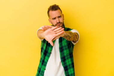 Sarı arka planda izole edilmiş genç dövmeli beyaz adam elini uzatmış, dur işareti göstererek seni engelliyor..