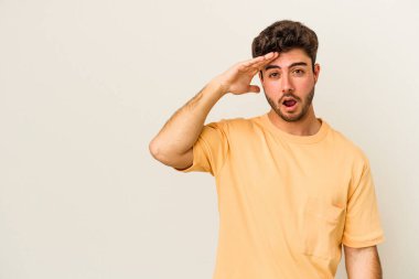 Beyaz arka planda izole edilmiş genç beyaz bir adam uzaklara bakıyor ve elini alnına koyuyor..