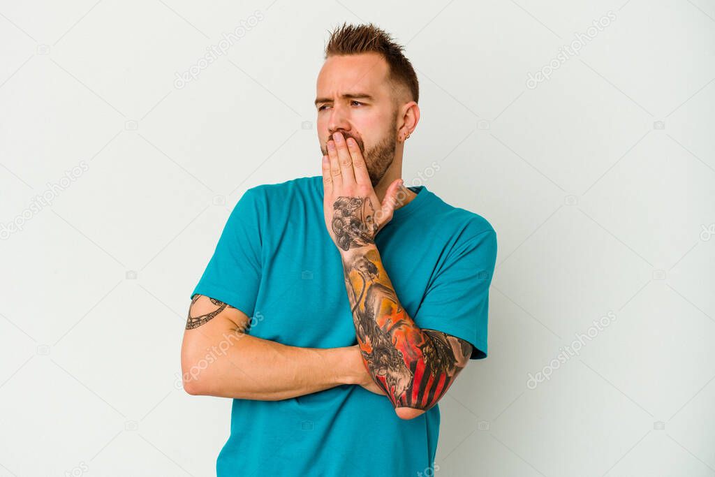 Young tattooed caucasian man isolated on white background yawning showing a tired gesture covering mouth with hand.
