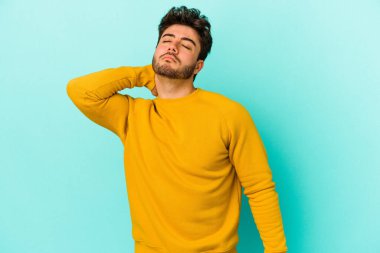 Kafkasyalı genç adam mavi arka planda izole edilmiş. Stres yüzünden boynu ağrıyor. Masaj yapıyor ve elle dokunuyor..