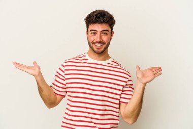 Beyaz arka planda izole genç beyaz adam kollarıyla ölçek yapar, mutlu ve kendinden emin hisseder..