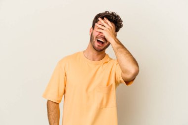 Beyaz arka planda soyutlanmış beyaz tenli genç bir adam elleriyle gözlerini kapatıyor, geniş bir gülümsemeyle bir sürpriz bekliyor..