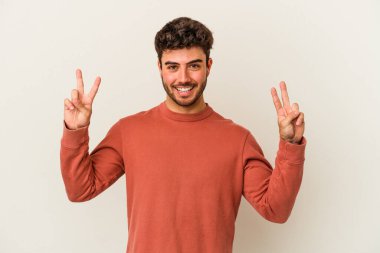 Beyaz arka planda izole edilmiş genç beyaz bir adam zafer işareti gösteriyor ve gülümsüyor..