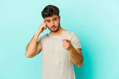 Mavi arka planda izole edilmiş genç beyaz bir adam şakağı parmağıyla işaret ediyor, düşünüyor ve bir göreve odaklanıyor..