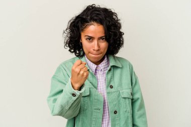 Beyaz arka planda izole edilmiş genç kıvırcık Latin kadın kameraya yumruk sallıyor, agresif yüz ifadesi var..