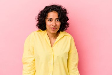 Pembe arka planda soyutlanmış genç kıvırcık Latin kadın omuzlarını silkeliyor ve gözleri açık..