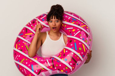 Beyaz arka planda izole edilmiş şişirilebilir bir donut tutan genç melez kadının bir fikri var, ilham verici bir kavram..