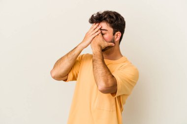 Beyaz arka planda izole edilmiş genç beyaz bir adam elleriyle gözlerini kapatmaktan korkuyor..