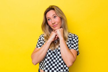 Avustralyalı genç bir kadın yalnız, elleri çenesinin altında, mutlu bir şekilde yan tarafa bakıyor..