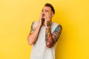 Genç dövmeli beyaz adam sarı arka planda izole edilmiş sızlanıyor ve ağlıyordu..