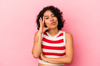 Pembe arka planda izole edilmiş genç kıvırcık Latin kadın yanakları patlatıyor, yorgun bir ifadesi var. Yüz ifadesi kavramı.