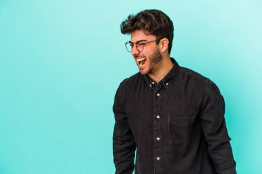 Kafkasyalı genç adam mavi arka planda izole edilmiş. Çok kızgın, öfkeli, hayal kırıklığına uğramış..