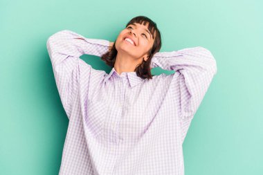 Genç melez kadın mavi üzerine izole edilmiş kendinden emin, elleri başının arkasında.