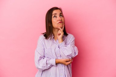 Orta yaşlı beyaz bir kadın pembe arka planda izole edilmiş düşünüyor ve yukarı bakıyor, yansıtıyor, düşünüyor, hayal kuruyor..