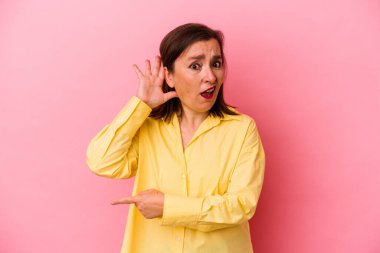 Orta yaşlı beyaz bir kadın pembe arka planda izole edilmiş bir şekilde bir dedikoduyu dinlemeye çalışıyor..