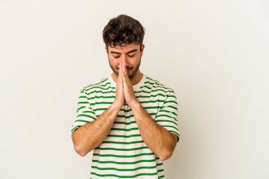 Beyaz arka planda izole edilmiş genç beyaz bir adam el ele tutuşup, ağız kenarında dua ediyor, kendinden emin..
