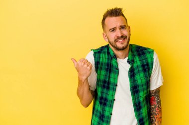 Sarı arka planda izole edilmiş genç dövmeli beyaz adam işaret parmağıyla fotokopi alanını işaret ederek şok oldu..