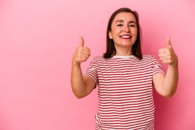 Orta yaşlı beyaz kadın pembe arka planda izole edilmiş gülümsüyor ve başparmağını kaldırıyor.