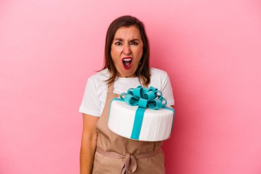 Orta yaşlı pasta şefi kadın mavi arka planda izole edilmiş bir pasta tutuyor. Çok sinirli ve agresif bağırıyor..