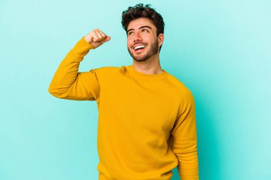 Mavi arka planda izole edilmiş genç beyaz bir adam zaferi, tutkuyu ve coşkuyu kutluyor, mutlu bir ifade..