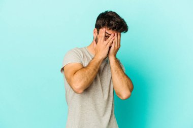 Kafkasyalı genç adam mavi arka planda izole edilmiş. Korkmuş ve gergin parmaklarıyla göz kırp..