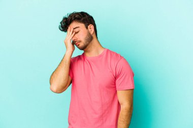 Kafkasyalı genç bir adam mavi arka planda izole edilmiş, başı ağrıyor, yüzüne dokunuyor..