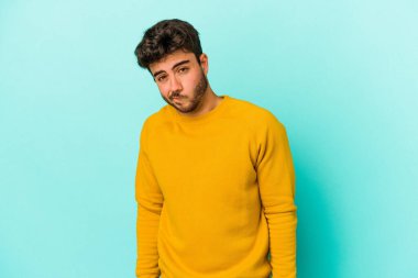 Mavi arka planda izole edilmiş genç beyaz adam omuzlarını silkeliyor ve gözleri açık..