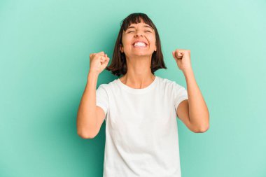 Genç melez kadın mavi üzerine izole edilmiş zaferi, tutkuyu ve coşkuyu kutluyor, mutlu bir ifade..