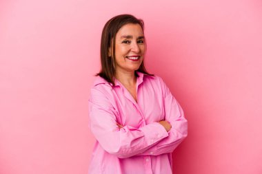 Pembe arka planda soyutlanmış orta yaşlı beyaz bir kadın. Kendine güveniyor, kararlılıkla kollarını kavuşturuyor..