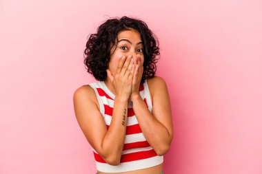 Genç kıvırcık Latin kadın pembe arka planda izole edilmiş şok olmuş, ağzı ellerle kaplanmış, yeni bir şey keşfetmeye hevesli..