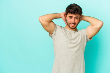 Kafkasyalı genç adam mavi arka planda izole edilmiş kafasının arkasına dokunuyor, düşünüyor ve bir seçim yapıyor..