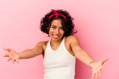 Pembe arka planda soyutlanmış genç kıvırcık Latin kadın hoş bir yüz ifadesi sergiliyor.