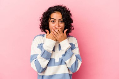 Pembe arka planda izole edilmiş genç kıvırcık Latin kadın elleriyle ağzını kapatırken şok oldu..