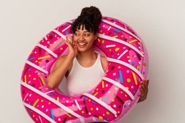 Beyaz arka planda izole edilmiş şişme bir donut tutan genç bir ırk kadını bir dedikoduyu dinlemeye çalışıyor..