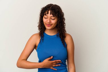 Beyaz arka planda soyutlanmış genç melez kadın karnına dokunuyor, nazikçe gülümsüyor, yemek yiyor ve tatmin oluyor..