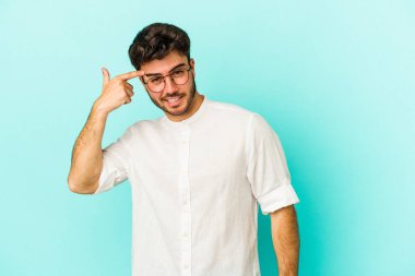 Mavi arka planda izole edilmiş genç beyaz adam işaret parmağıyla bir hayal kırıklığı jesti gösteriyor..
