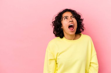 Pembe arka planda izole edilmiş genç kıvırcık Latin kadın çok kızgın, öfkeli, hayal kırıklığına uğramış.