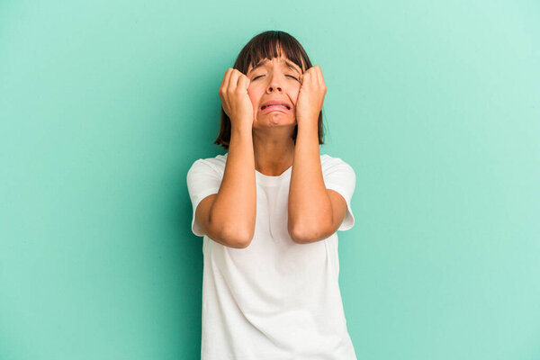 Young mixed race woman isolated on blue crying, unhappy with something, agony and confusion concept.