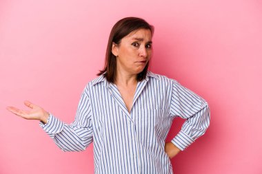 Orta yaşlı, beyaz bir kadın pembe arka planda izole edilmiş sorgulama sırasında omuz silkiyor ve kuşkulanıyor..