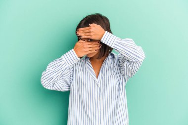 Genç melez kadın mavi ışıkta izole olmuş parmaklarıyla kameraya bakıyor, yüzünü kapatmaktan utanıyor..