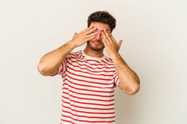 Beyaz arka planda izole edilmiş genç beyaz bir adam elleriyle gözlerini kapatmaktan korkuyor..