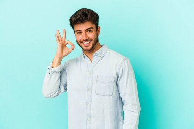 Kafkasyalı genç adam mavi arka planda izole edilmiş neşeli ve kendinden emin..