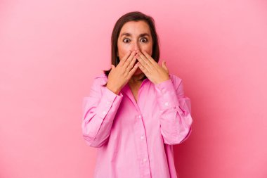 Orta yaşlı beyaz kadın pembe arka planda izole edilmiş. Şok olmuş, ağzı ellerle kaplanmış, yeni bir şey keşfetmeye hevesli..