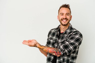 Beyaz arka planda izole edilmiş beyaz dövmeli genç bir beyaz adam palmiye ağacında bir kopya alanı tutuyor..