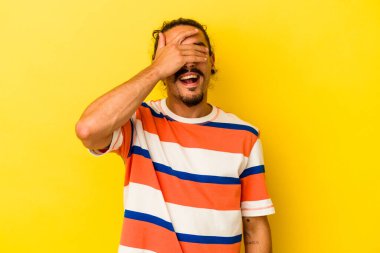 Sarı arka planda izole edilmiş uzun saçlı, genç beyaz bir adam. Gözleri ellerle kaplıyor. Gülümsüyor ve bir sürpriz bekliyor..