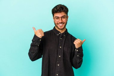 Kafkasyalı genç adam mavi arka planda izole edilmiş. Baş parmağını kaldırıyor, gülümsüyor ve kendinden emin..