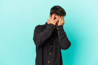 Kafkasyalı genç adam mavi arka planda izole edilmiş. Korkmuş ve gergin parmaklarıyla göz kırp..