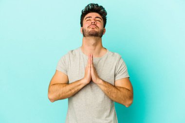 Mavi arka planda izole edilmiş genç beyaz bir adam el ele tutuşup, ağzının kenarında dua ediyor, kendinden emin..